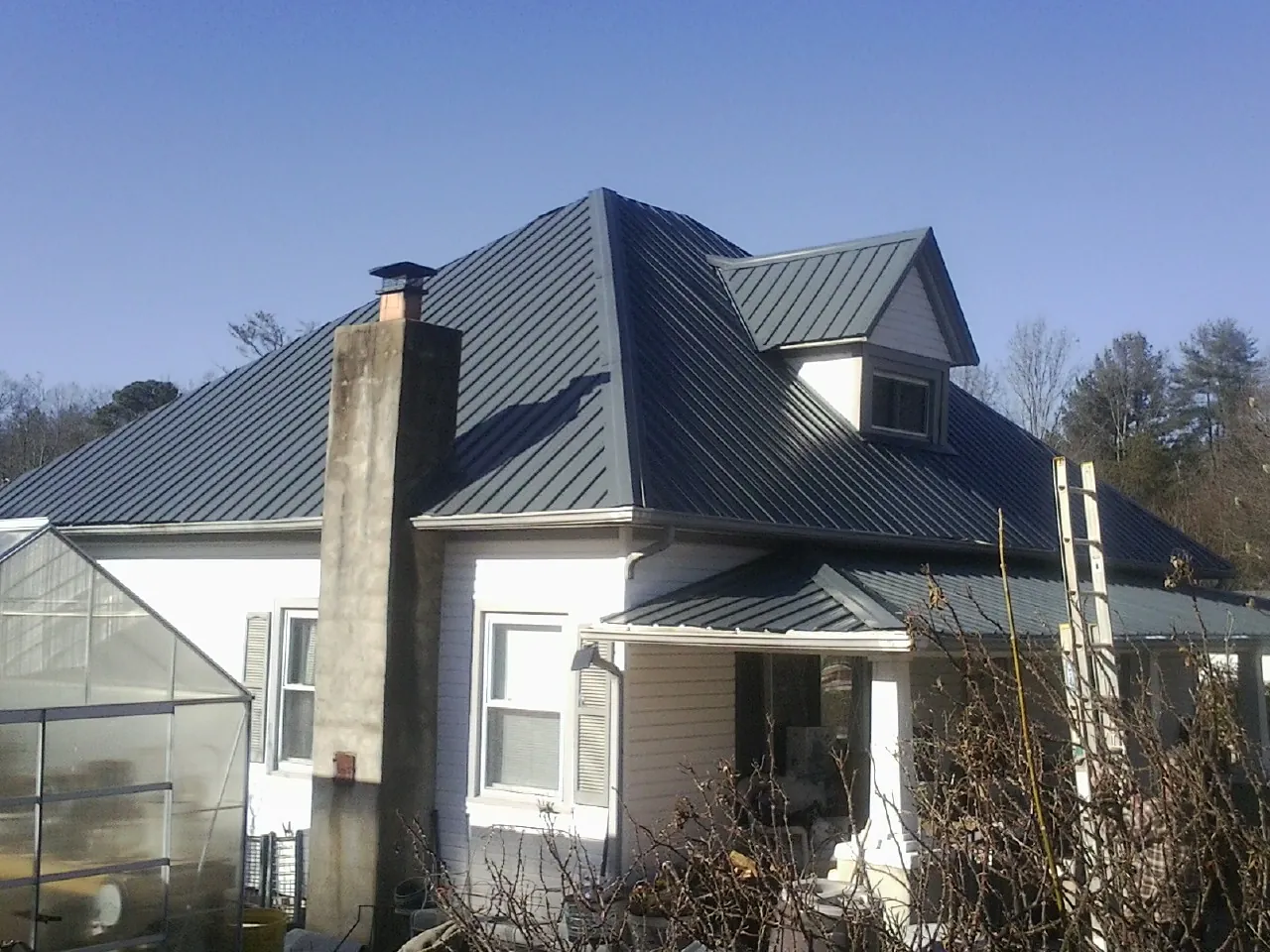 Dark blue standing seam metal roof on a white farmhouse with dormer — Slate & Tile Roof Repair by Roofing Brothers in Rochester Mills
