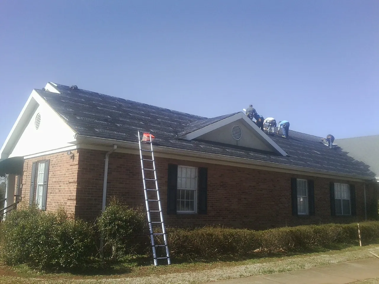 Crew tearing shingles off a brick ranch roof with a ladder set — Emergency Roof Repair work by our crew in Rochester Mills
