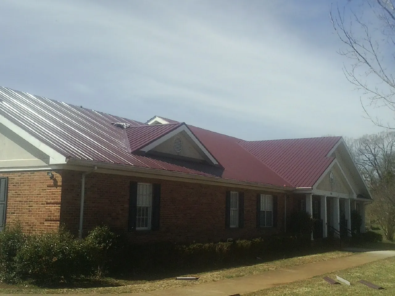 Red metal roof with gabled entries on a long brick building, from a Hail Damage Roof Repair job in Rochester Mills
