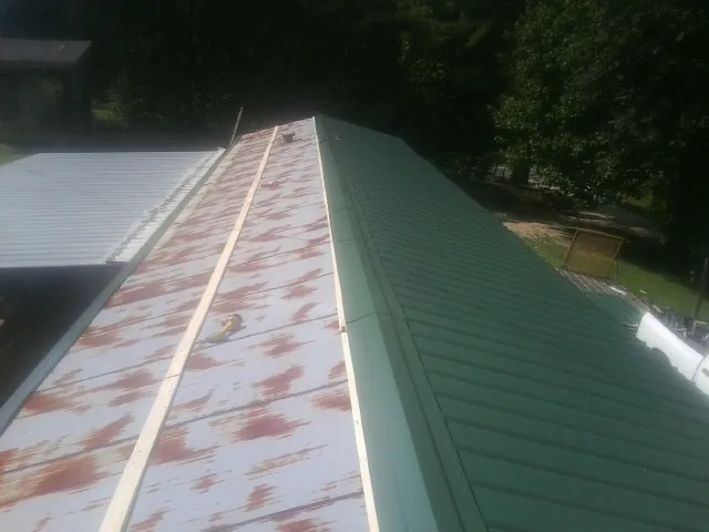 Old rusted panels beside newly installed green metal roofing — Wind Damage Roof Repair by Roofing Brothers in Rochester Mills