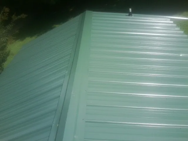 New green metal panels meeting at the ridge of a roof — Flat Roof Repair work by our crew in Rochester Mills