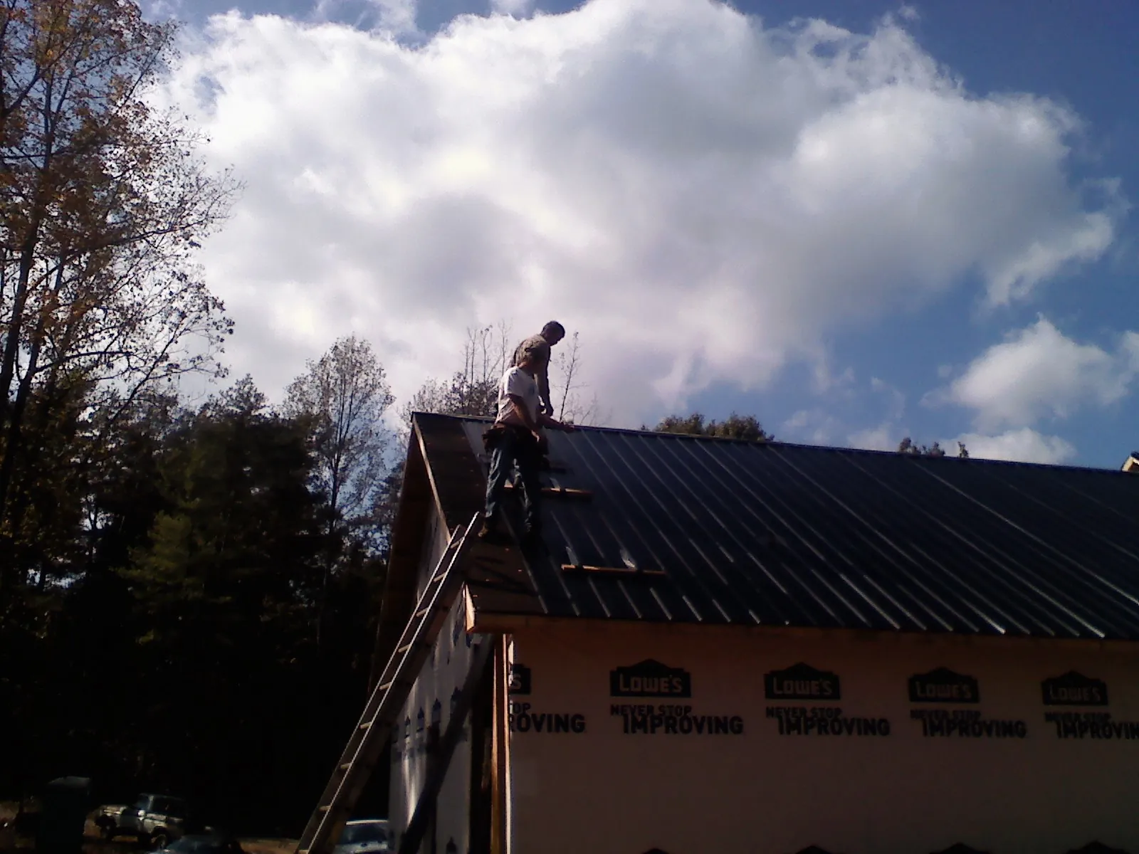 Roofer fastening dark metal panels high against a cloudy sky, from a Roof Inspection job in Rochester Mills