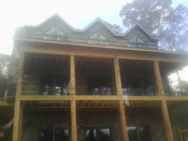 Dormers and porch framing on a large log home under construction — Roof Coating work by our crew in Rochester Mills