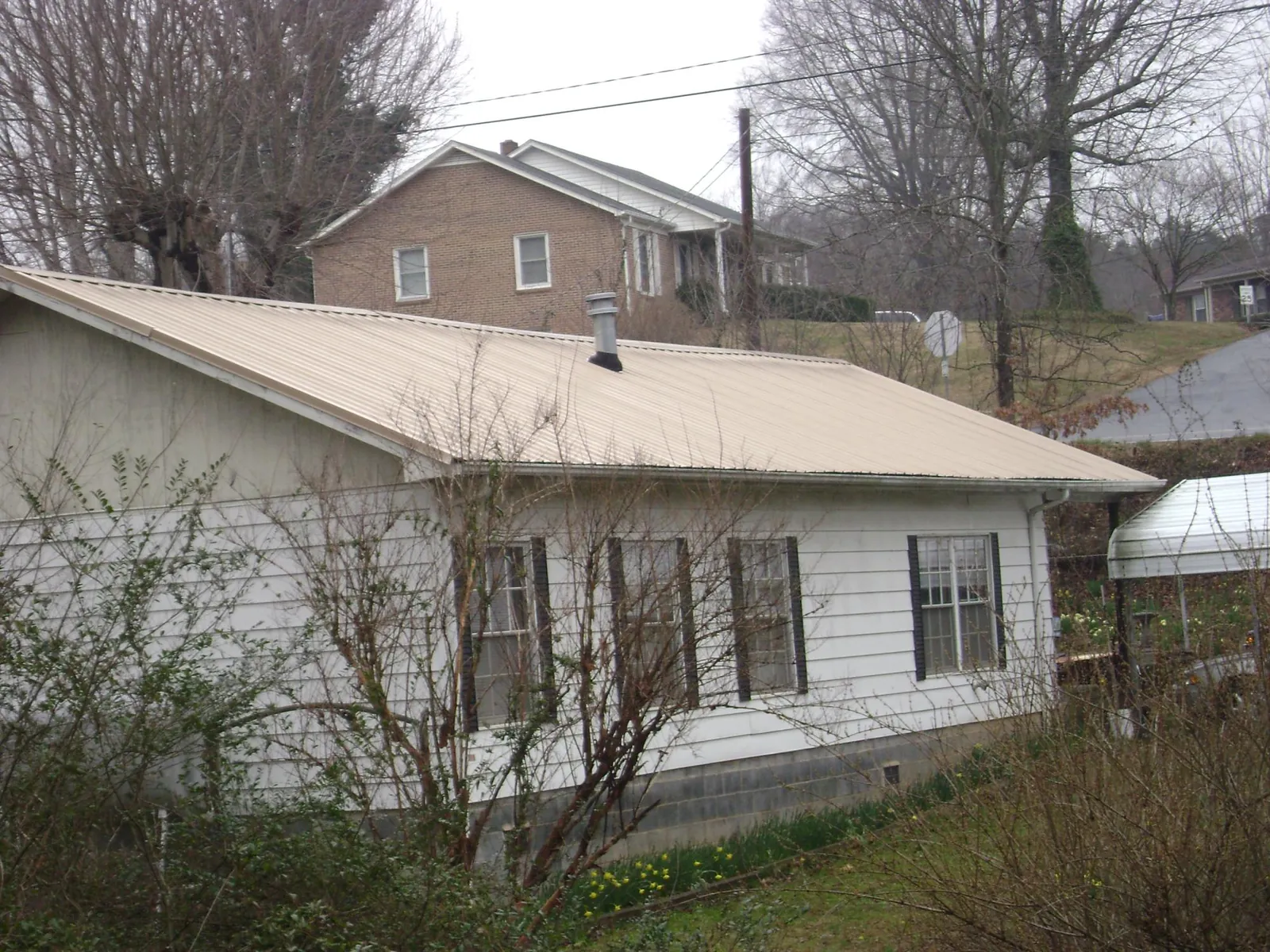 Tan metal roof on a white sided house set into a hillside — Commercial Roofing by Roofing Brothers in Rochester Mills