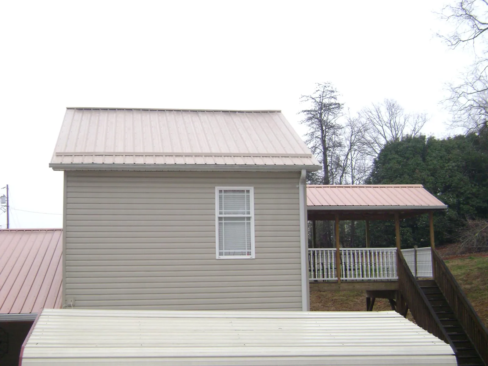Tan metal roofs on a two story addition and attached porch, from a Roof Replacement job in Rochester Mills